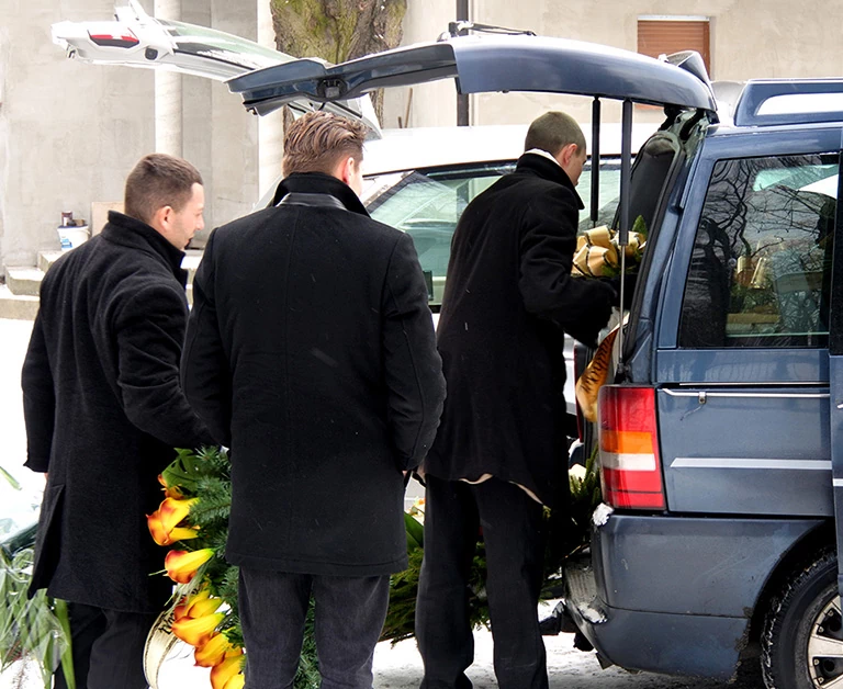 Ludzie stojący przy samochodzie pogrzebowym