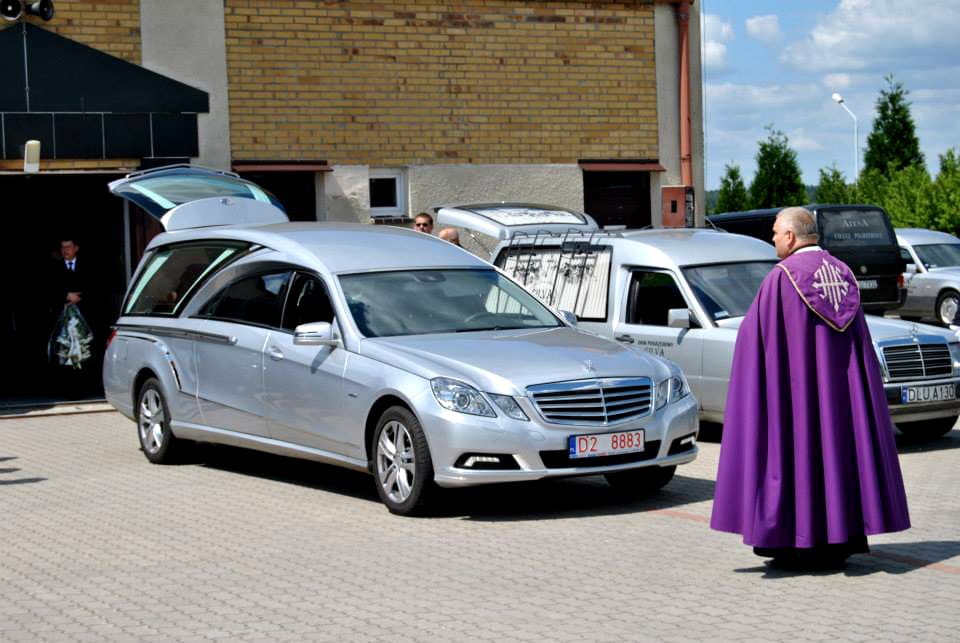 Ksiądz stojący przy samochodzie pogrzebowym